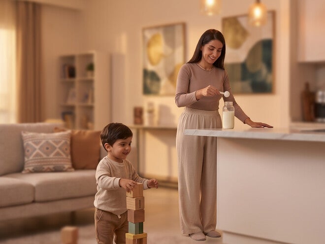 Photograph: mother pouring milk at kitchen island while toddler stacks wooden blocks.